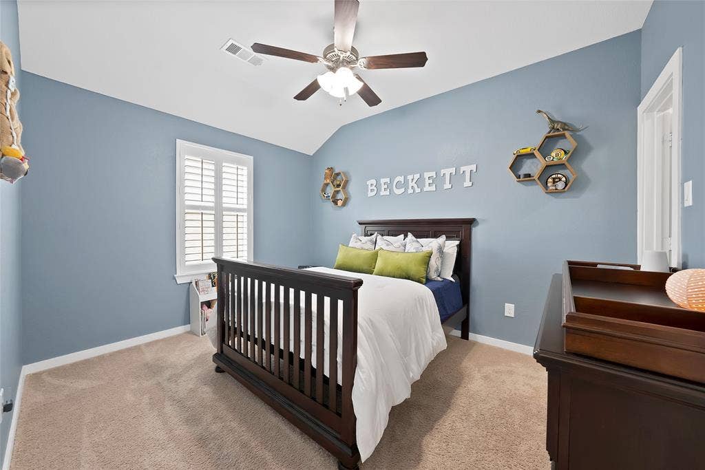 Carpeted room featuring a vaulted ceiling with a ceiling fan, a window with white louvered shutters, and light blue walls