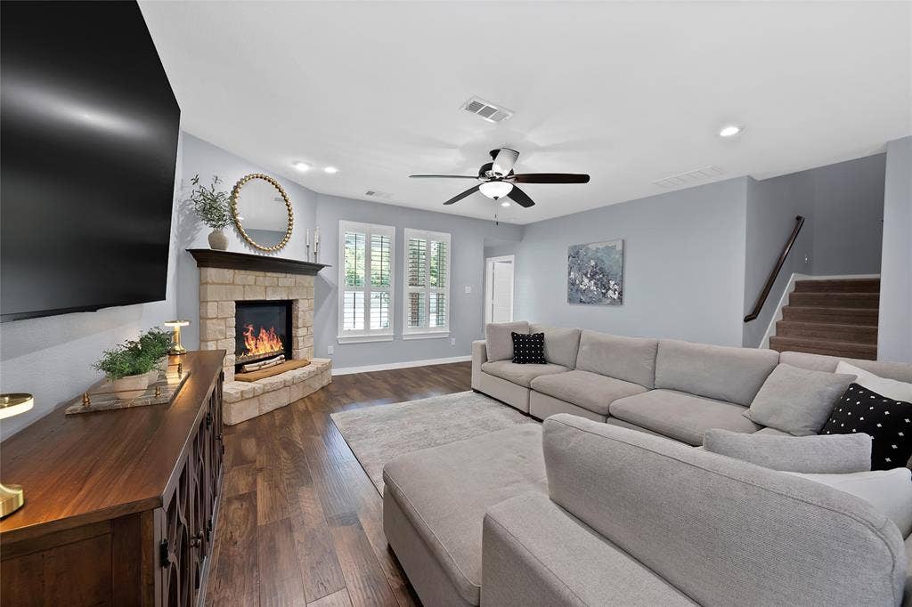 Living area featuring wood-finish flooring, a stone-faced corner fireplace with a dark mantel, and plantation shutters on the windows