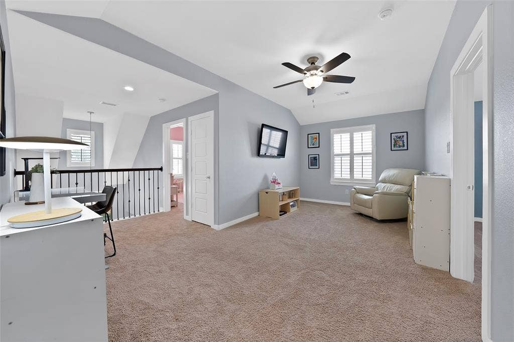 Spacious upper-level loft featuring vaulted ceilings, a ceiling fan with integrated lighting, and carpeted flooring