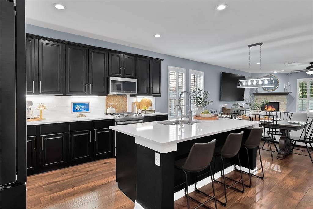 Modern kitchen featuring an oversized island with seating, dark shaker cabinetry, stainless steel appliances, white subway tile backsplash, and wood-finish flooring
