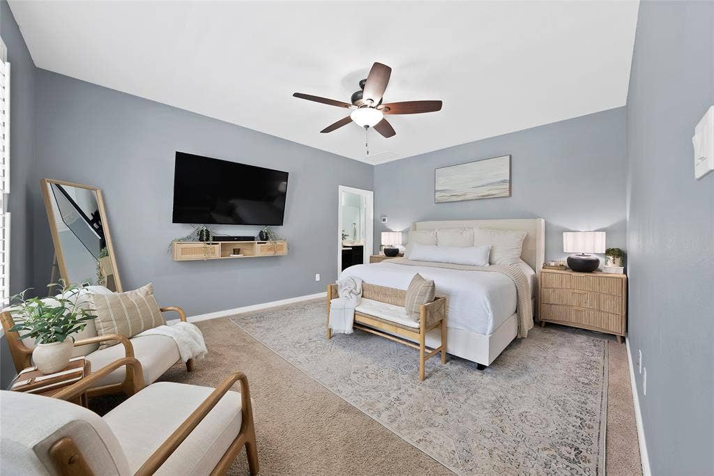 Spacious bedroom featuring light blue walls, wood-finish ceiling fan, and carpet flooring
