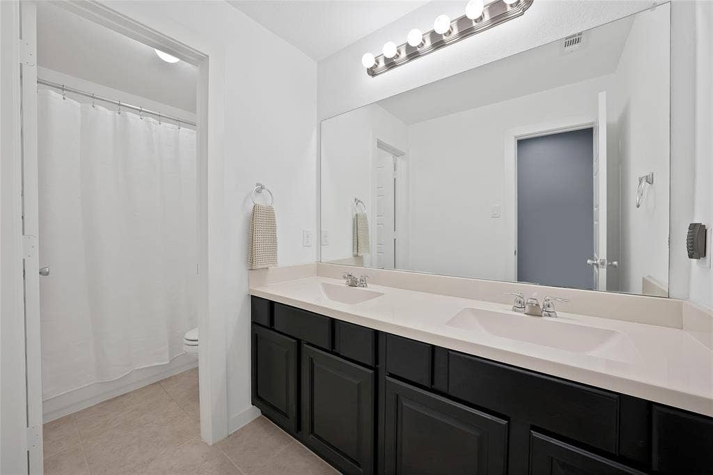 Bathroom featuring a dual vanity with dark cabinetry, light countertops, and chrome fixtures