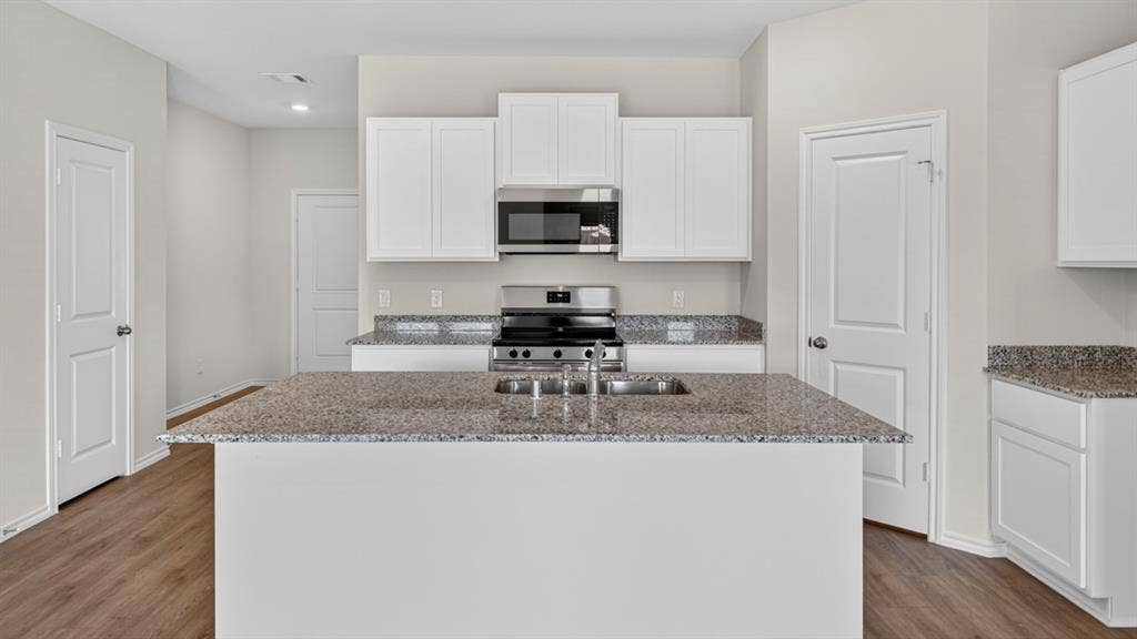 6053 Freedom Drive, Lindale, TX 75771 Kitchen featuring a central island with an undermount sink, granite countertops, white cabinetry, stainless steel appliances, and wood-finish flooring