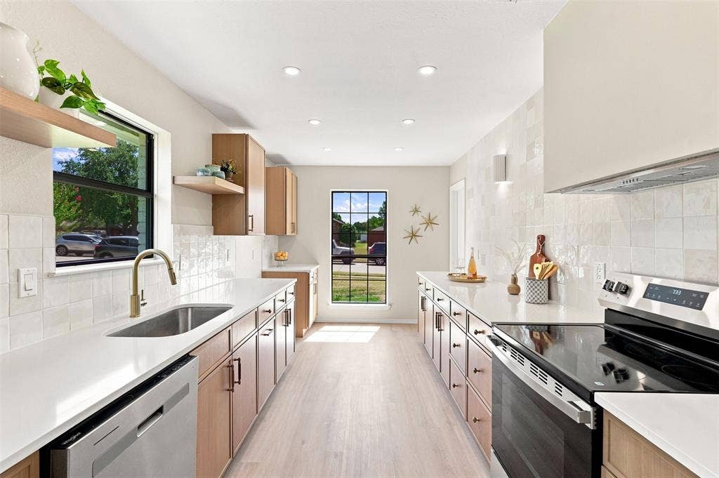 7321 Burke Circle, Plano, TX 75025 Galley kitchen featuring light wood-finish cabinetry, light countertops, integrated sink with a gooseneck faucet, stainless steel appliances, and wood-finish flooring