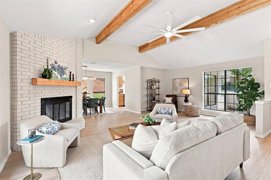 7321 Burke Circle, Plano, TX 75025 Vaulted ceiling with exposed wood beams, light wood-finish flooring, white brick fireplace, black-framed windows, and an open-concept layout