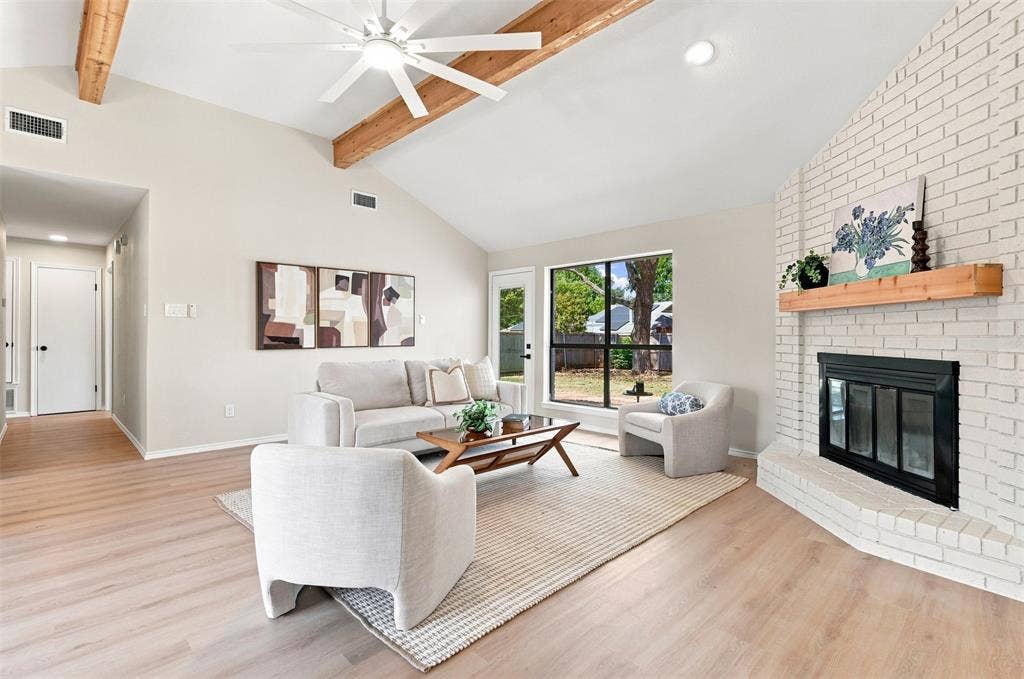 7321 Burke Circle, Plano, TX 75025 Vaulted ceiling with exposed wood beams and ceiling fan, wood-finish flooring, white brick fireplace with wood mantel, and large window with exterior access