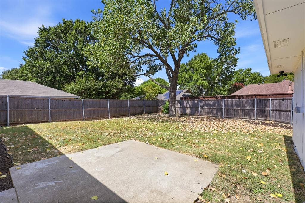 7321 Burke Circle, Plano, TX 75025 Spacious backyard with a large concrete patio, mature tree, and wood privacy fencing
