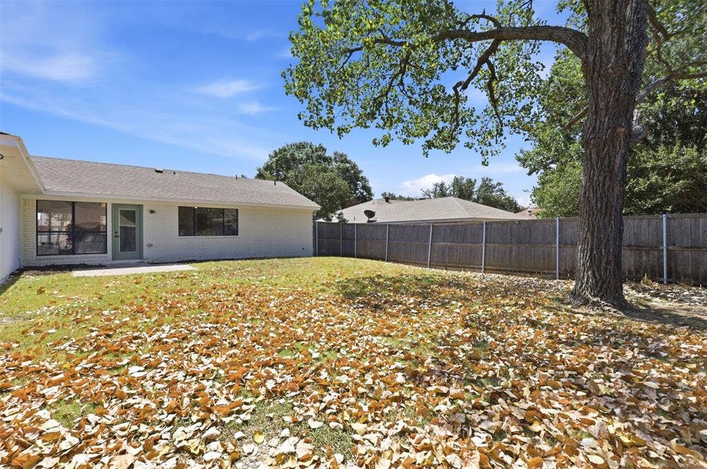 7321 Burke Circle, Plano, TX 75025 Expansive backyard featuring a mature tree, wood privacy fencing, a concrete patio, and a light-colored exterior with multiple windows