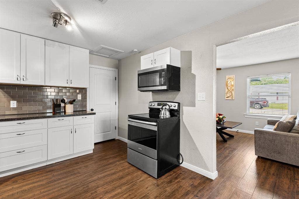 3700 Charlton Avenue, Waco, TX 76711 Kitchen featuring white cabinetry, dark countertops, a metallic subway tile backsplash, stainless steel appliances, and wood-finish flooring