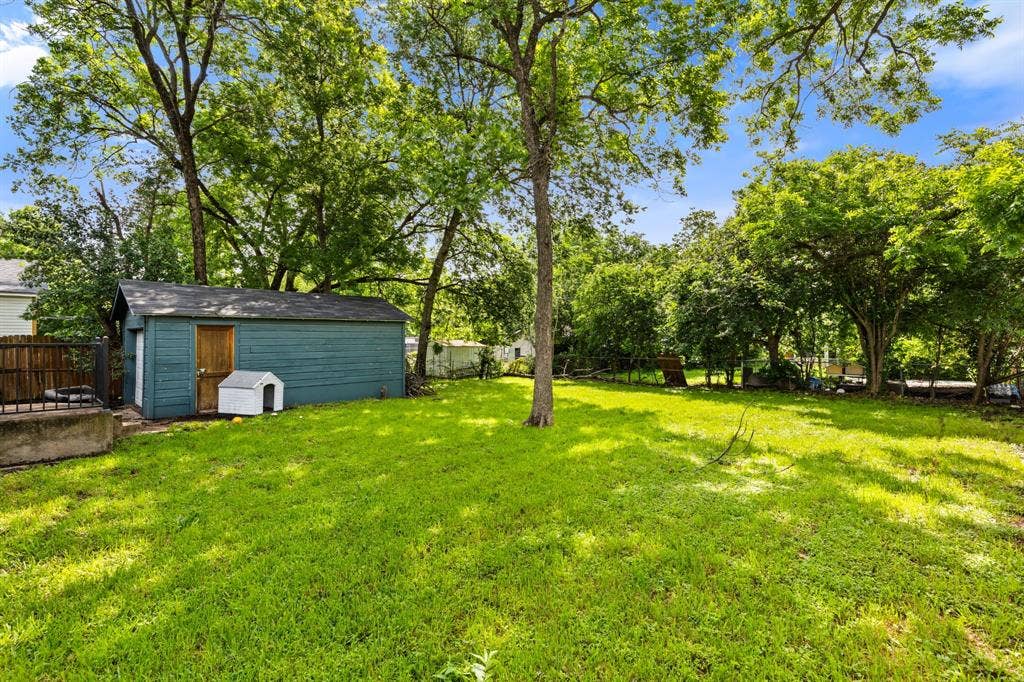 3700 Charlton Avenue, Waco, TX 76711 Expansive green lawn featuring mature trees, a blue exterior shed with a brown door, and a partial wooden fence