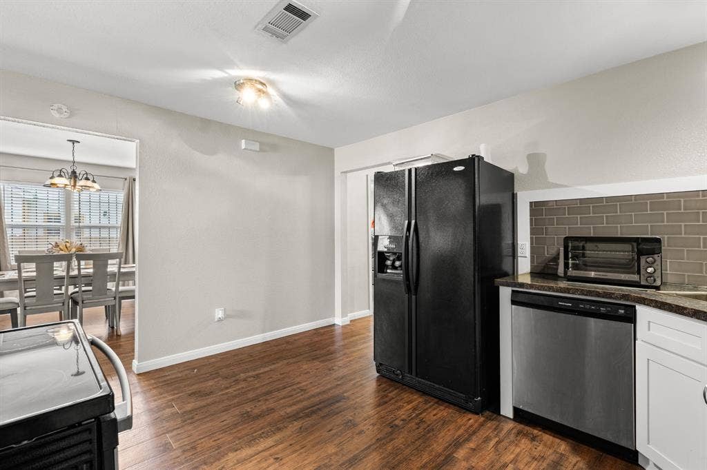 3700 Charlton Avenue, Waco, TX 76711 Kitchen featuring wood-finish flooring, white cabinetry, a dark subway tile backsplash, and a stainless-steel dishwasher