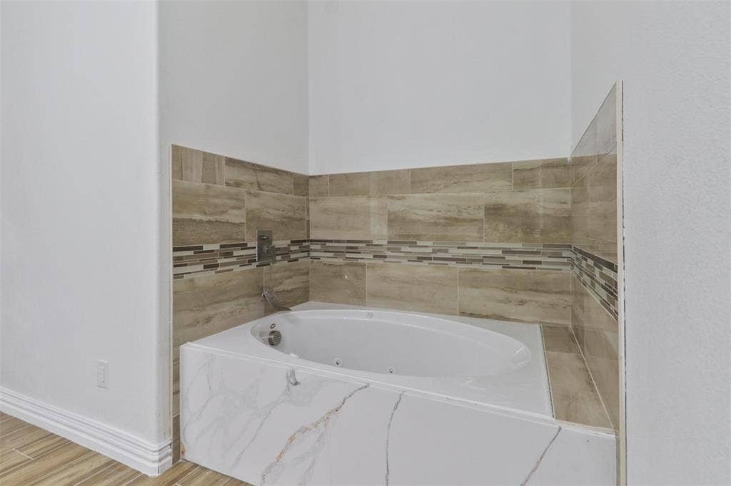 4112 Balch Drive, Dallas, TX 75216 Spa-inspired primary bathroom featuring a freestanding soaking tub with integrated deck surround, horizontal wood-finish tile walls in warm neutral tones, and a coordinating tile accent stripe