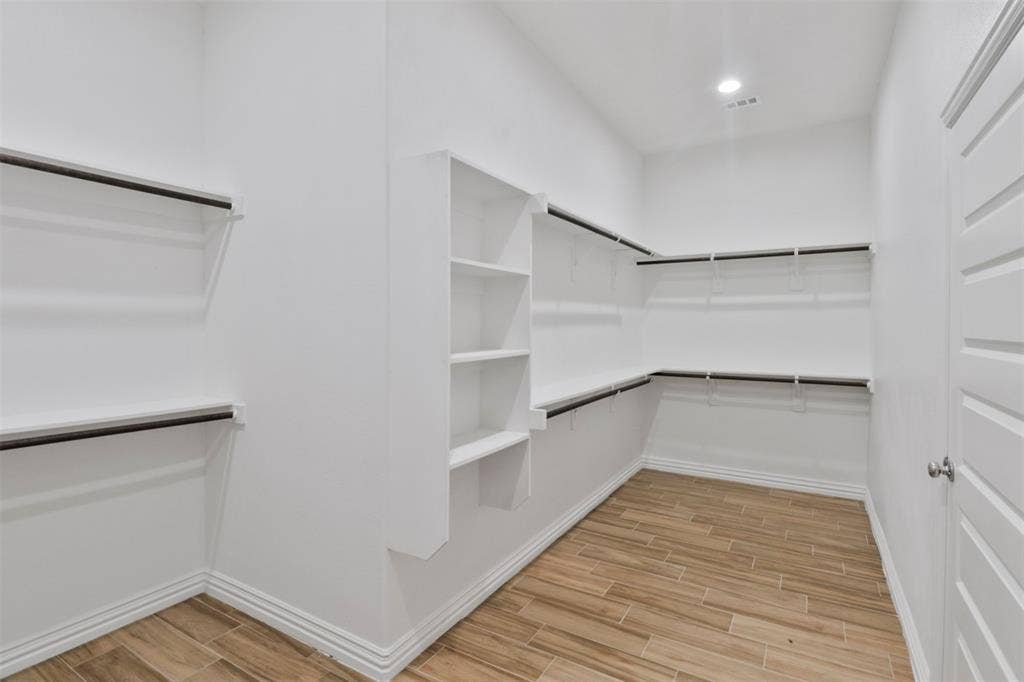 4112 Balch Drive, Dallas, TX 75216 Spacious walk-in closet featuring wood-finish flooring, extensive built-in shelving, multiple hanging rods, recessed lighting, and a paneled interior door