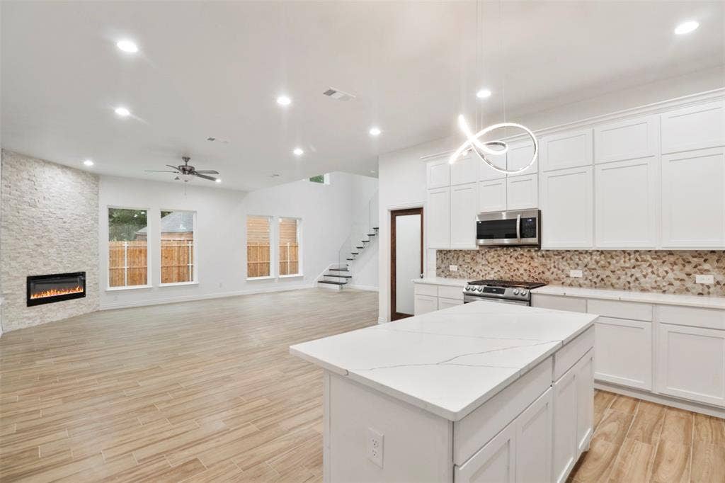 4112 Balch Drive, Dallas, TX 75216 Open-concept living space featuring a chef's kitchen with white cabinetry, quartz waterfall island countertop, stainless steel appliances, and a tile backsplash