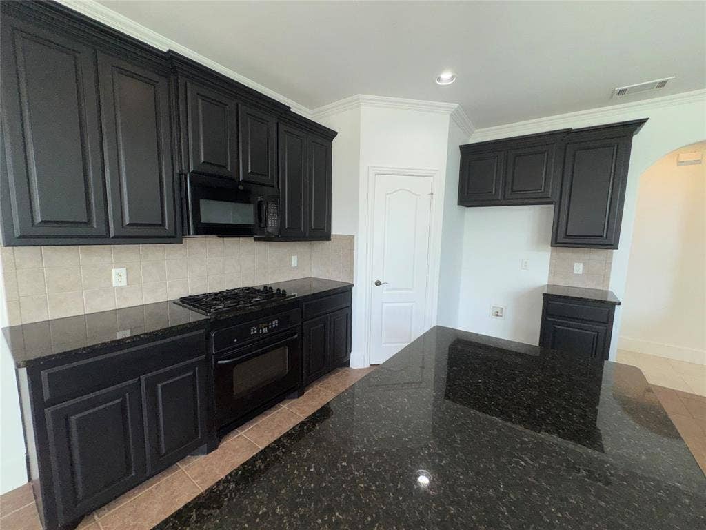 1913 Lawnview Drive, McKinney, TX 75072 Modern kitchen featuring dark cabinetry with recessed panel detailing, stainless steel gas range and built-in microwave, subway tile backsplash, and a spacious dark stone countertop with waterfall edge