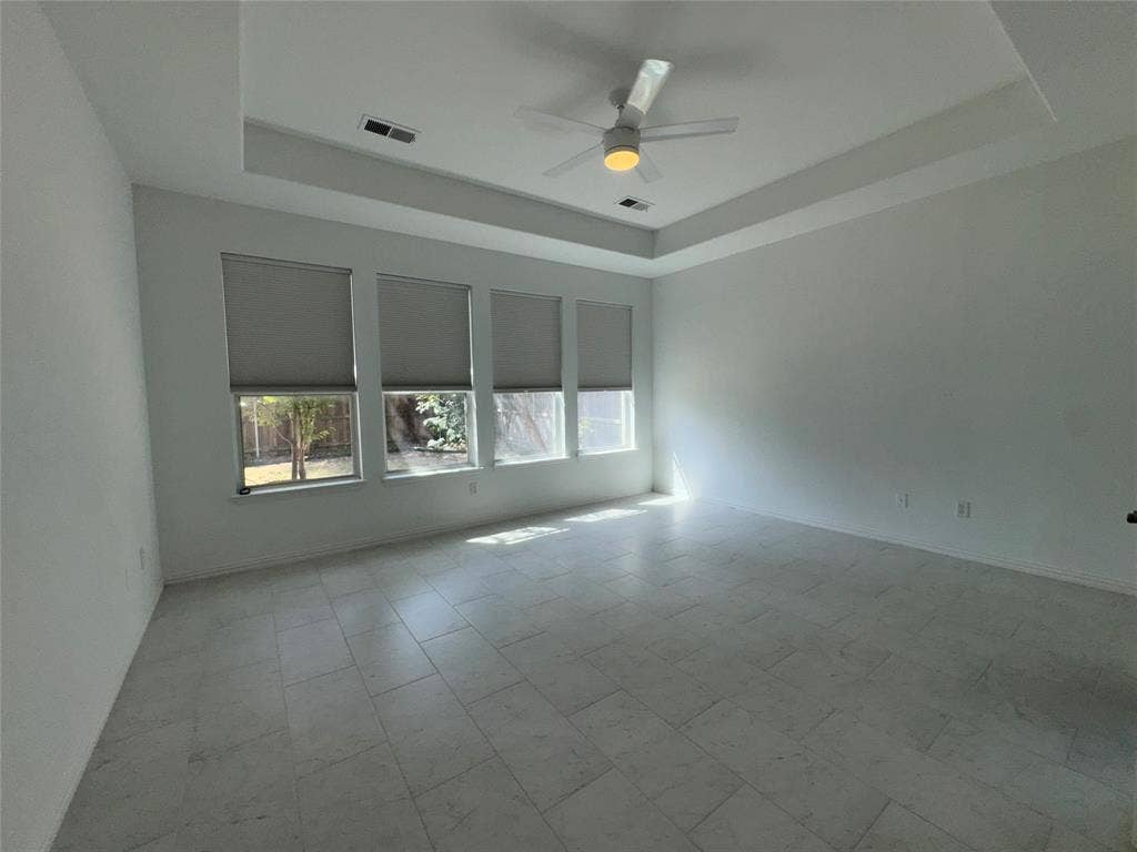 1913 Lawnview Drive, McKinney, TX 75072 Spacious interior featuring a tray ceiling with a modern ceiling fan, large rectangular tile flooring, and a wall of three windows with roller shades