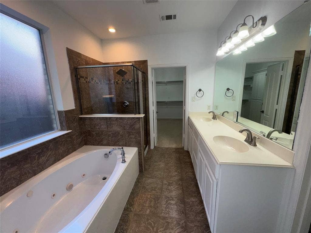 1913 Lawnview Drive, McKinney, TX 75072 Spa-inspired master bathroom featuring a luxurious whirlpool soaking tub with glass enclosure, dual-sink vanity with white cabinetry and brushed nickel fixtures, large framed mirror with integrated lighting, and wood-finish flooring throughout