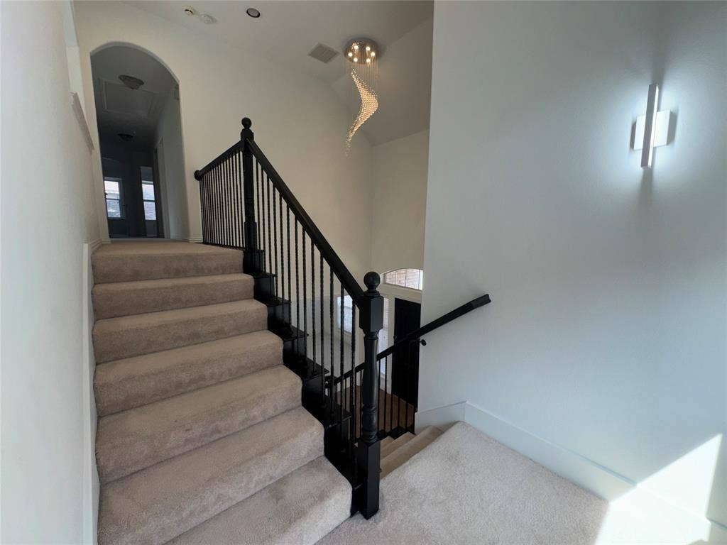 1913 Lawnview Drive, McKinney, TX 75072 Elegant staircase featuring neutral-toned carpeted treads, black metal railings with turned balusters, and a gracefully arched architectural entryway