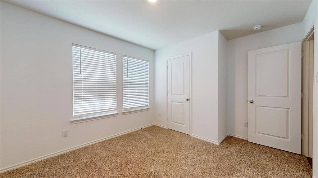 717 Cottonwood Way, Royse City, TX 75189 Carpeted room with white walls, two windows featuring horizontal blinds, and two panel doors with chrome hardware