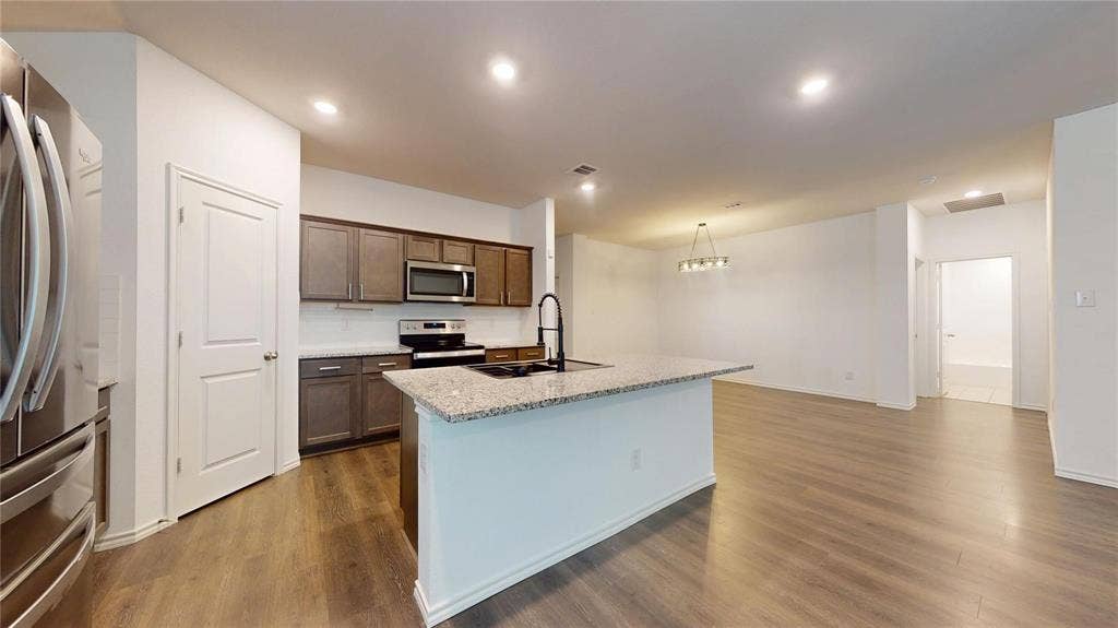 717 Cottonwood Way, Royse City, TX 75189 Open-concept kitchen and dining area featuring a spacious island with a stone-finish countertop, dark wood-finish cabinetry, stainless steel appliances, and wood-finish flooring