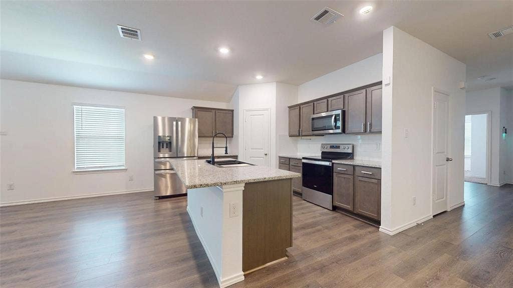 717 Cottonwood Way, Royse City, TX 75189 Modern kitchen featuring an island with a light-toned countertop, stainless steel appliances, dark wood-finish cabinetry, and a white subway tile backsplash