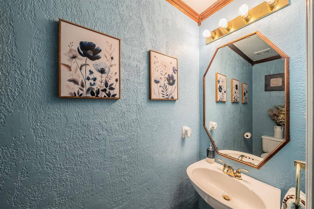 812 Chaparral Drive, Grand Prairie, TX 75052 Pedestal sink with brass-finish faucet, an octagonal mirror, and overhead vanity lighting