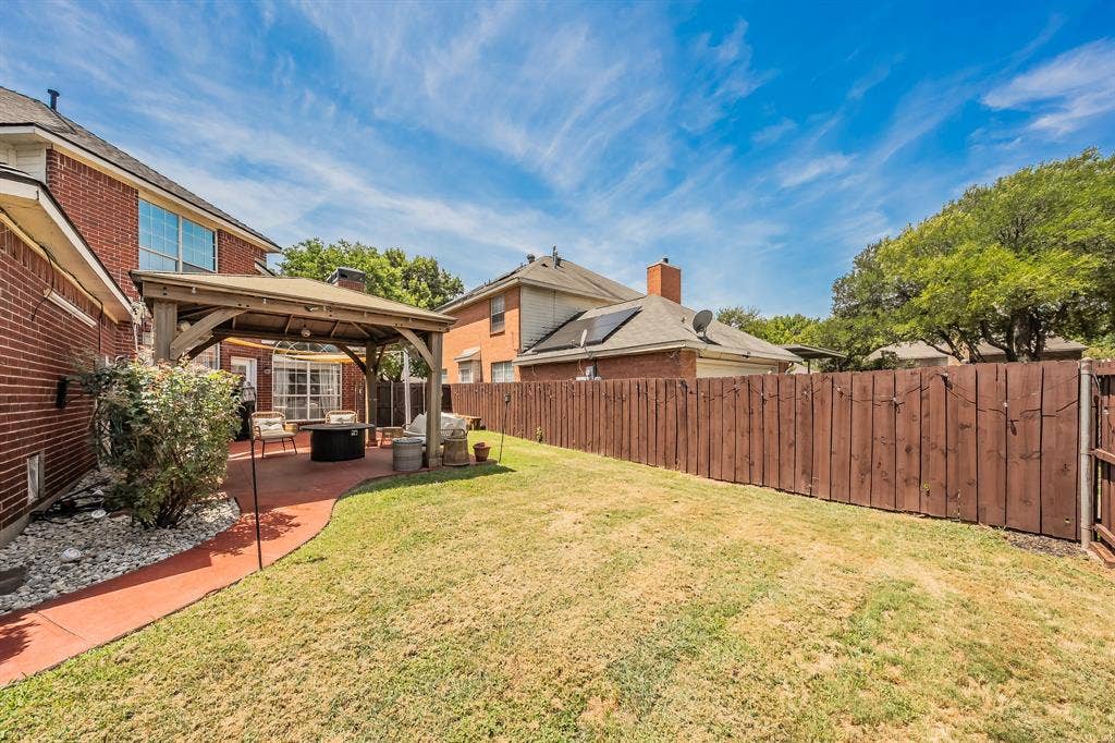 812 Chaparral Drive, Grand Prairie, TX 75052 Expansive backyard featuring a large green space, a red concrete patio, a wooden gazebo, and a tall privacy fence