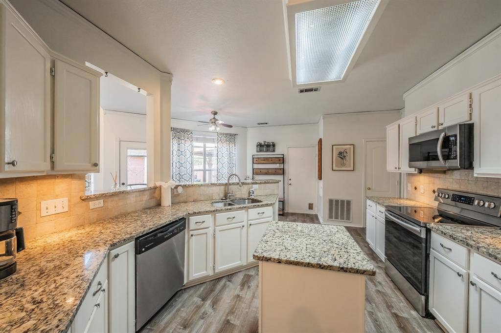 812 Chaparral Drive, Grand Prairie, TX 75052 Kitchen featuring a central island, wood-finish flooring, white cabinetry, granite countertops, and stainless steel appliances