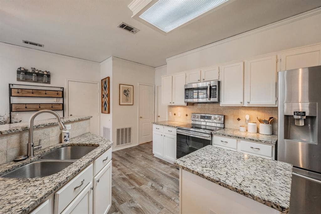 812 Chaparral Drive, Grand Prairie, TX 75052 Kitchen featuring white cabinetry, wood-finish flooring, stainless steel appliances, granite countertops, and a tile backsplash