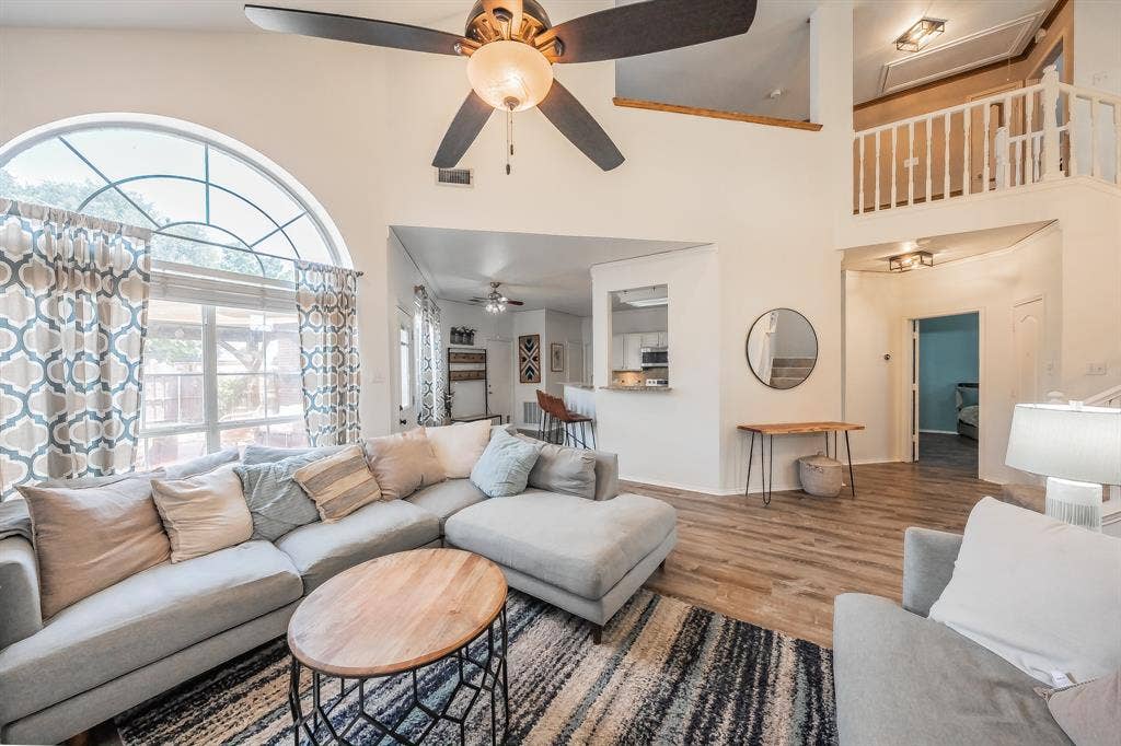 812 Chaparral Drive, Grand Prairie, TX 75052 Great room featuring vaulted ceilings, an arched picture window, wood-finish flooring, an upper-level balcony with white railings, and a ceiling fan with integrated lighting