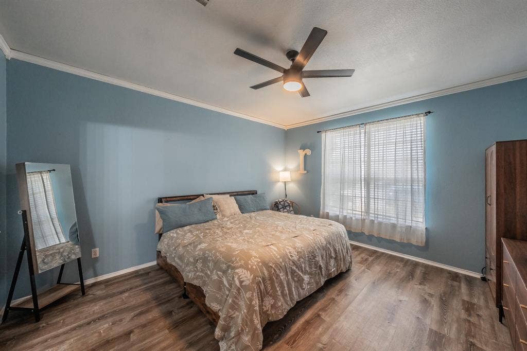 812 Chaparral Drive, Grand Prairie, TX 75052 Bedroom featuring blue walls, white crown molding, wood-finish flooring, a window with blinds and sheer curtains, and a ceiling fan with integrated lighting