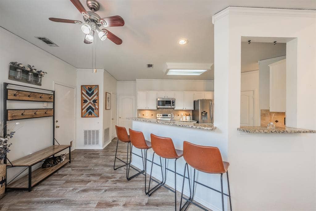 812 Chaparral Drive, Grand Prairie, TX 75052 Open-concept living area featuring wood-finish flooring, a ceiling fan with integrated lighting, and a breakfast bar with a granite countertop