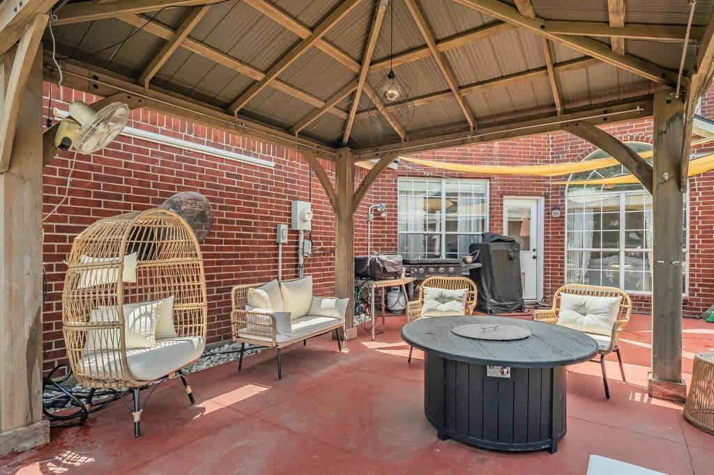 812 Chaparral Drive, Grand Prairie, TX 75052 Covered patio featuring a wood-frame gazebo with a corrugated metal roof, red brick exterior walls, and a red-toned concrete slab