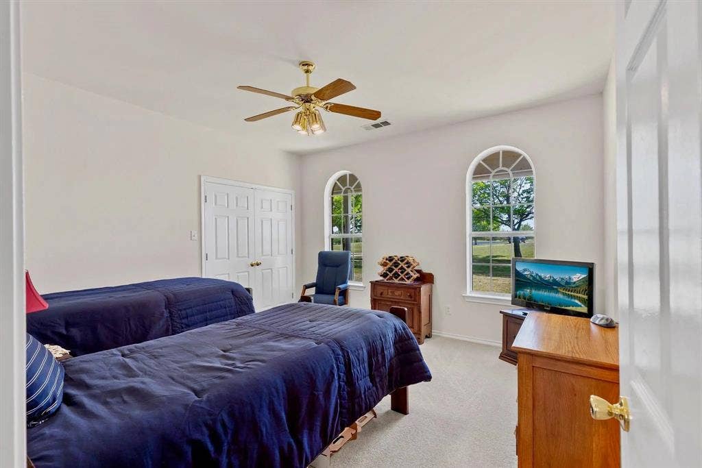 Spacious room featuring two arched windows with intricate upper grille work, a ceiling fan with integrated lighting, and carpeted flooring
