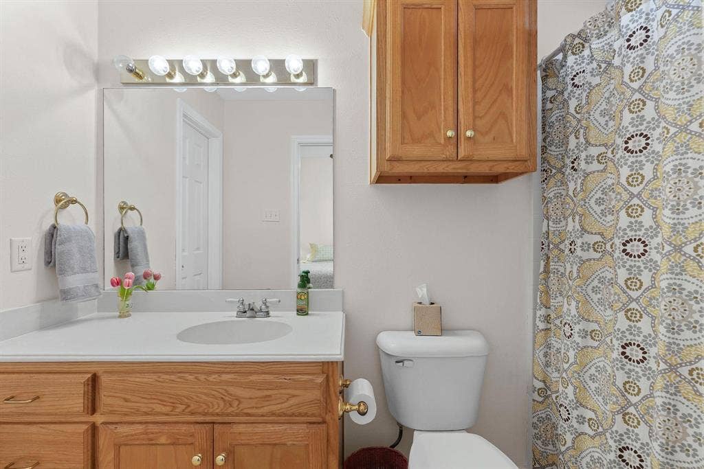 Bathroom featuring a wood-finish vanity with a light-colored countertop, an undermount sink, and a large mirror with strip lighting