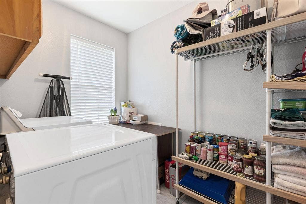 Laundry area featuring two white appliances, a window with horizontal blinds, and upper cabinetry
