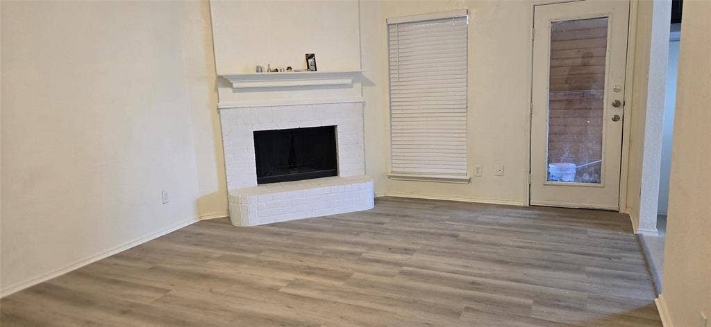 4809 Orchard Ridge Drive, Garland, TX 75043 Living area featuring wood-finish flooring, a white brick fireplace with mantel, and a glass-paneled door