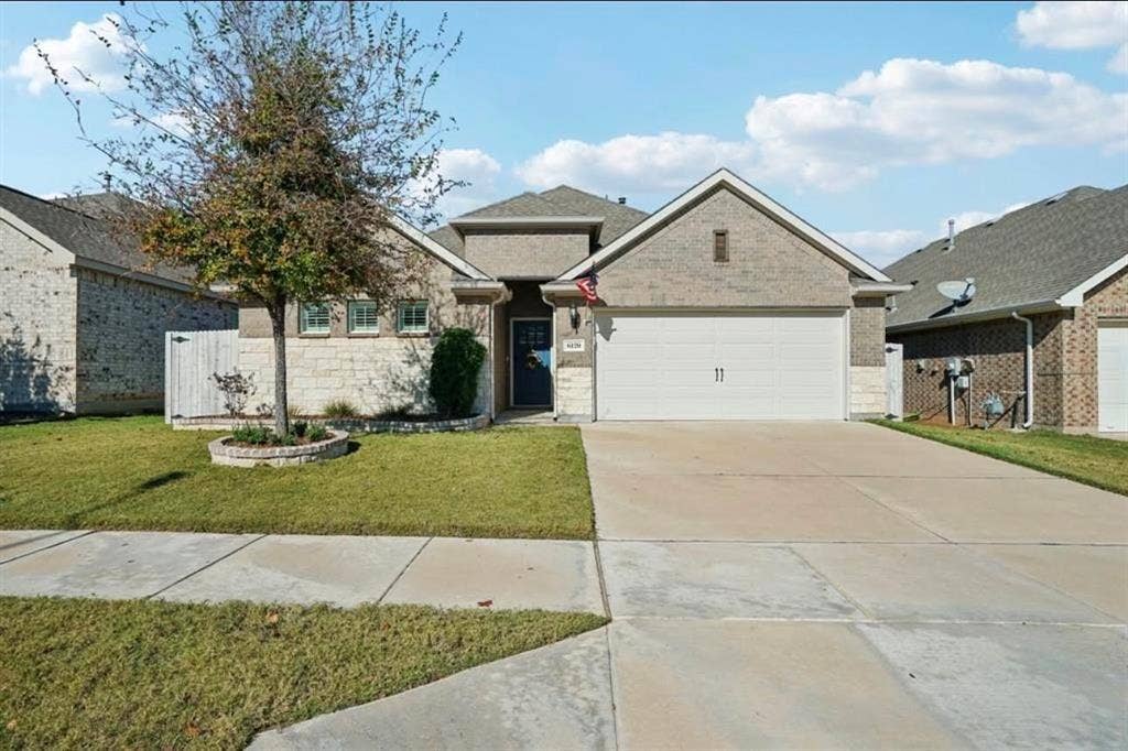 Fort Worth, TX 76123 Brick and stone facade residence featuring a two-car garage, concrete driveway, and front lawn with a single tree in a raised planter