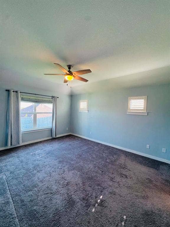 Fort Worth, TX 76123 Expansive carpeted room featuring a ceiling fan with integrated lighting, multiple windows with blinds and curtains, and light blue wall finishes