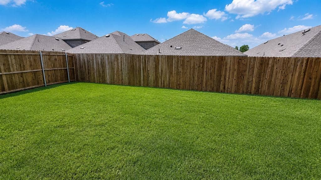 1317 crookpost Drive, Princeton, TX 75407 Expansive backyard featuring a lush green lawn, full wood fencing, and a clear sky overhead