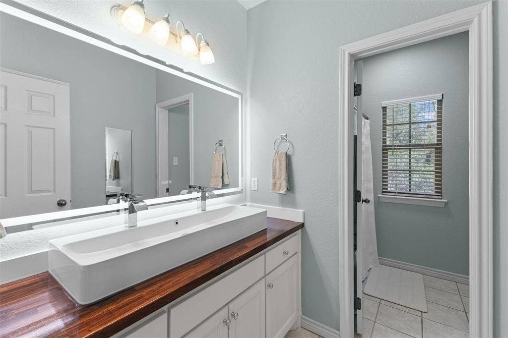 325 Bolton Road, Granbury, TX 76049 Vanity with a wood-finish countertop, dual vessel sinks, and an illuminated mirror