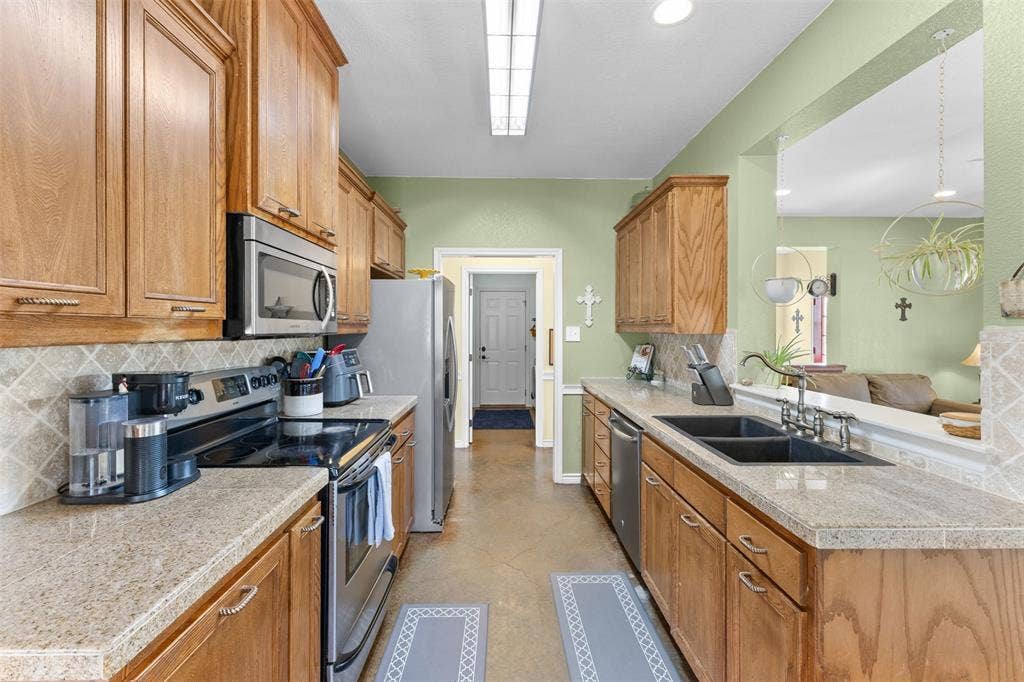 325 Bolton Road, Granbury, TX 76049 Galley kitchen featuring wood cabinetry, stone-finish countertops, stainless steel appliances, a tile backsplash, and a pass-through opening