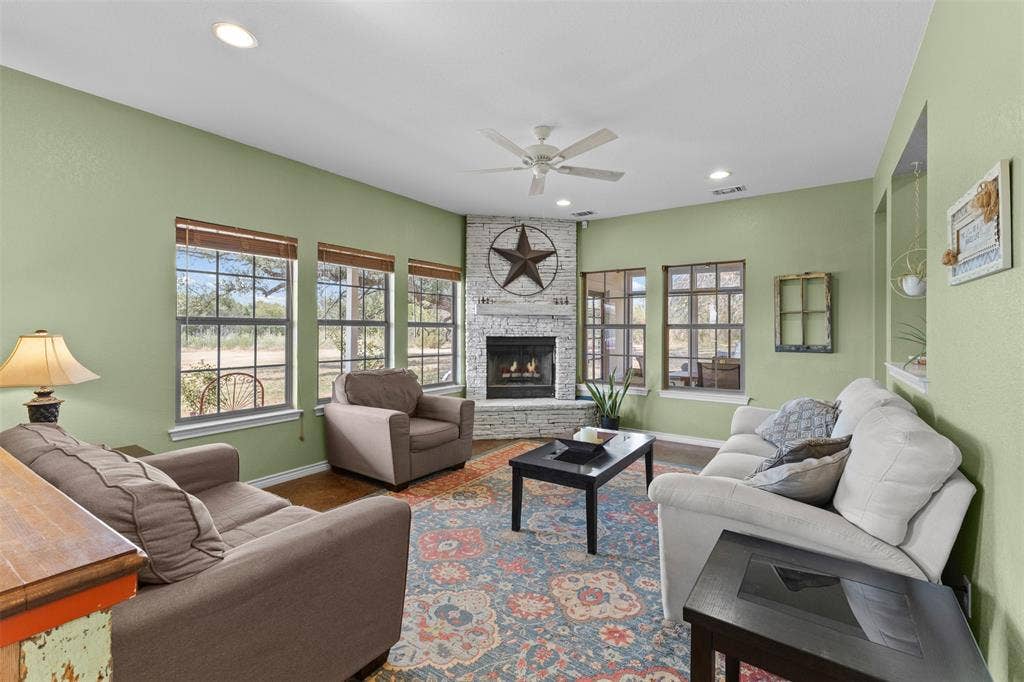 325 Bolton Road, Granbury, TX 76049 Corner fireplace with stone surround, recessed lighting, ceiling fan, multiple windows with grid panes, and built-in wall niches