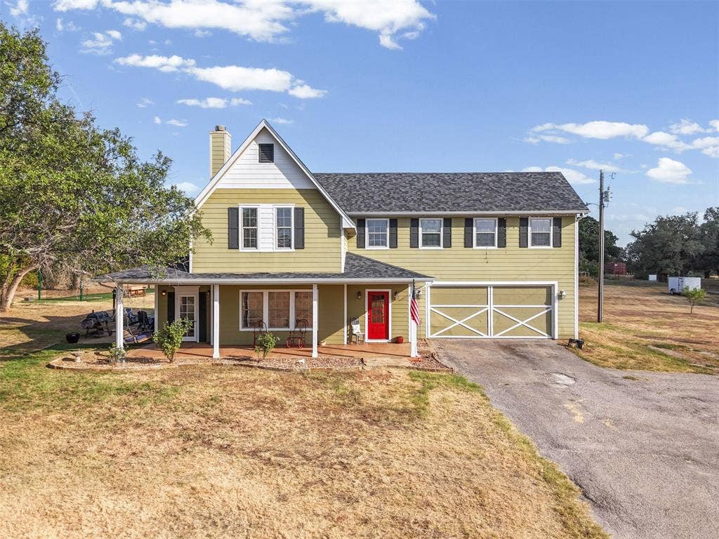 325 Bolton Road, Granbury, TX 76049 Two-story residence featuring a covered front porch, attached garage with decorative doors, and a prominent gable roofline