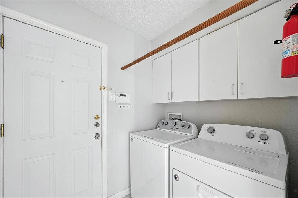 Dedicated laundry room featuring side-by-side washer and dryer units, white cabinetry with ample storage, neutral countertop workspace, and direct access to the home's exterior