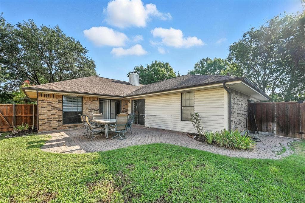 Charming single-story residence featuring a brick and siding exterior with a covered patio, mature landscaping with established trees, and a spacious manicured lawn