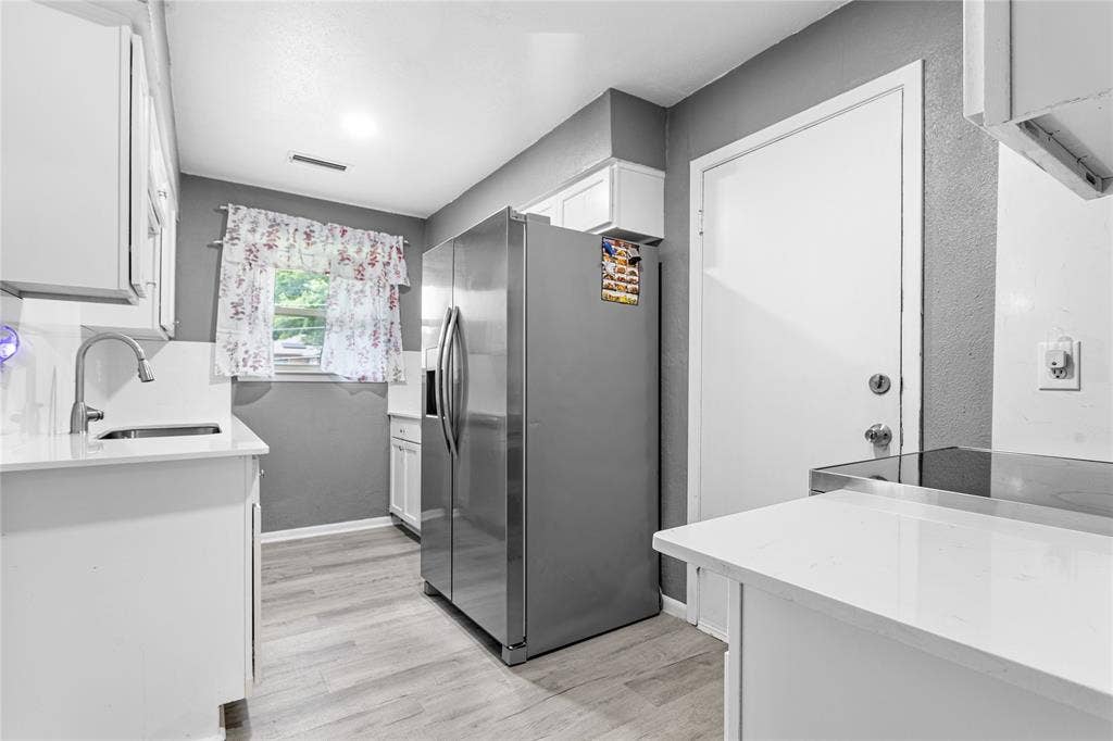 6930 Trailcrest Drive, Dallas, TX 75232 Kitchen featuring a stainless steel refrigerator, white cabinetry, light-toned countertops, wood-finish flooring, and a window