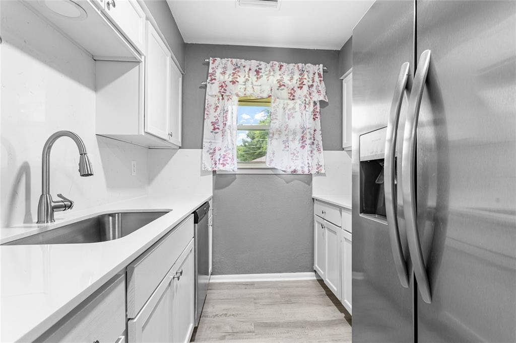6930 Trailcrest Drive, Dallas, TX 75232 Kitchen featuring white cabinetry, light-toned countertops, a stainless steel sink with a gooseneck faucet, a stainless steel refrigerator, and wood-finish flooring