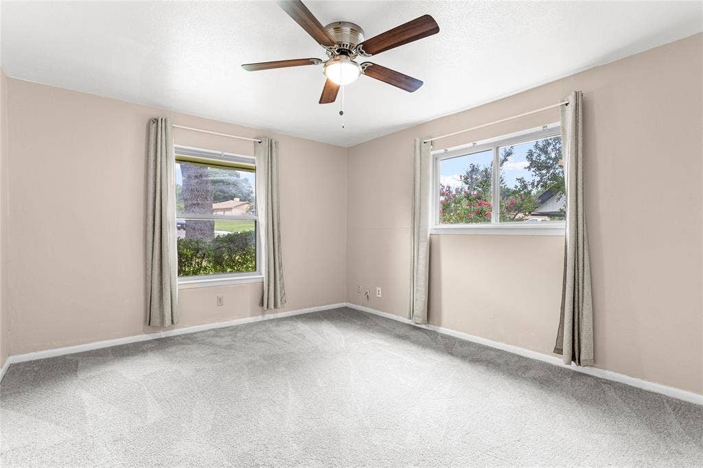 6930 Trailcrest Drive, Dallas, TX 75232 Spacious room featuring light-colored walls, grey carpeting, two windows, and a ceiling fan with wood-finish blades