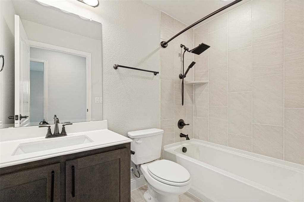 5405 Pooley Lane, McKinney, TX 75071 Bathroom featuring a dark wood-finish vanity with a white countertop and integrated sink, matte black fixtures, a white toilet, and a bathtub with light-toned tiled walls